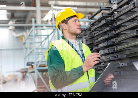 Lavoratore di indumenti da lavoro protettiva con appunti esaminando le parti in acciaio in fabbrica Foto Stock