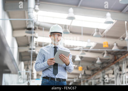 Ingegnere con hard-hat e tavoletta digitale a piedi in fabbrica Foto Stock