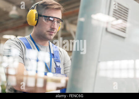 Lavoratore focalizzato in indumenti da lavoro protettiva al computer in fabbrica Foto Stock