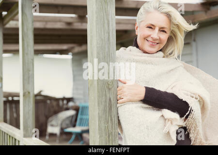 Ritratto sorridente senior donna che indossa scialle sul portico ventoso Foto Stock