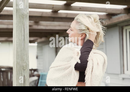 Senior donna con le mani nei capelli indossare scialle sul portico Foto Stock