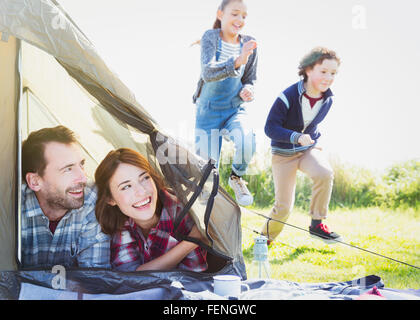 Coppia sorridente in tenda a guardare i bambini in esecuzione in erba Foto Stock