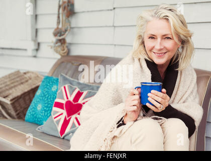 Ritratto sorridente donna senior di bere il caffè sul divano patio Foto Stock