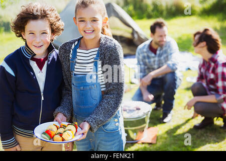 Ritratto sorridente fratello e sorella con gli spiedini di vegetali al campeggio Foto Stock