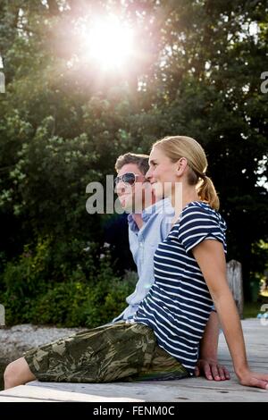 Giovane seduto sul molo in legno a Lakeside Foto Stock