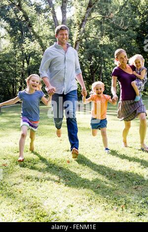 Matura in esecuzione e tenendo le mani con tre figlie in posizione di parcheggio Foto Stock