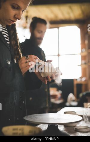 Vista laterale della giovane donna in officina la spazzolatura pentola di creta Foto Stock