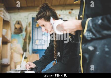 Vista laterale della giovane donna in officina di agitazione di smalto ceramico, guardando lontano Foto Stock