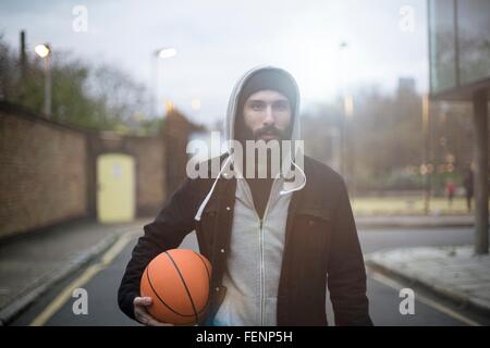 Ritratto di metà uomo adulto in street, tenendo la pallacanestro Foto Stock