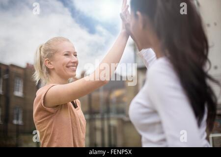 Due giovani donne dando alta cinque, all'aperto Foto Stock
