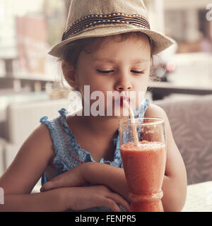 Divertimento kid ragazza in hat frullato di bere succo di vetro in street city cafe. Tonica closeup ritratto Foto Stock