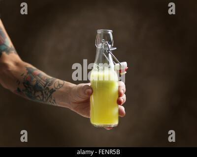 Tatuato womans braccio impugnando sugo greggio in una bottiglia di vetro Foto Stock