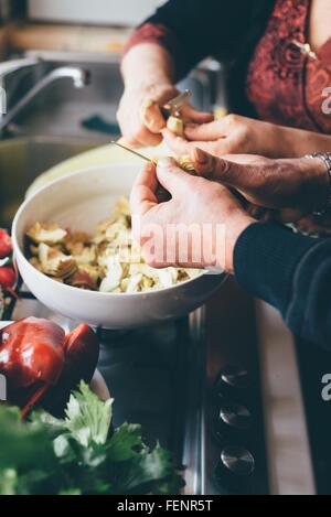 Maschio e femmina per affettare le mani carciofi in cucina Foto Stock