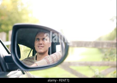 Ala di riflessione speculare del giovane uomo in auto parcheggiate al gate rurale Foto Stock