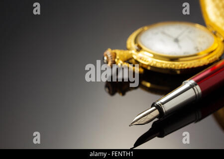 Orologio da tasca e a penna di inchiostro su sfondo nero Foto Stock
