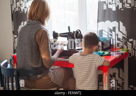 Donna e bambino figlio utilizzando vintage macchina da cucire sul tavolo di fronte alla finestra Foto Stock