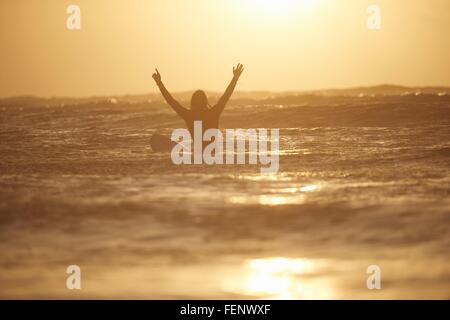 Silhouette di un giovane maschio del surfista con le braccia sollevate in mare, Devon, Inghilterra, Regno Unito Foto Stock