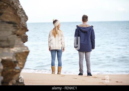 Vista posteriore della coppia giovane guardando fuori dalla spiaggia, Constantine Bay, Cornwall, Regno Unito Foto Stock