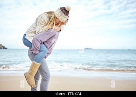 Giovane ragazza dando un piggyback sulla spiaggia, Constantine Bay, Cornwall, Regno Unito Foto Stock