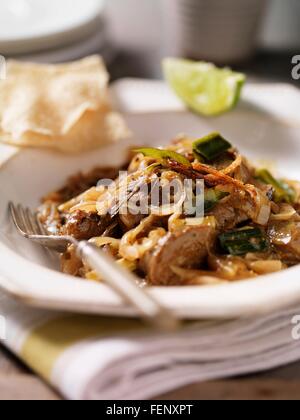 Ciotola di nero curry di agnello con cipolle, lime slice e papadums Foto Stock