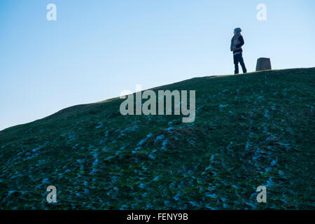 Donna in piedi vicino ad un pilastro di triangolazione, sulla parte superiore dell' antico tumulo, situato sulla cima di Garth Mountain, nord Foto Stock