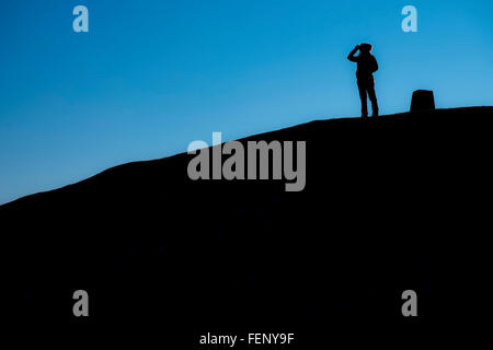 Donna in piedi vicino ad un pilastro di triangolazione, sulla parte superiore dell' antico tumulo, situato sulla cima di Garth Mountain, nord Foto Stock