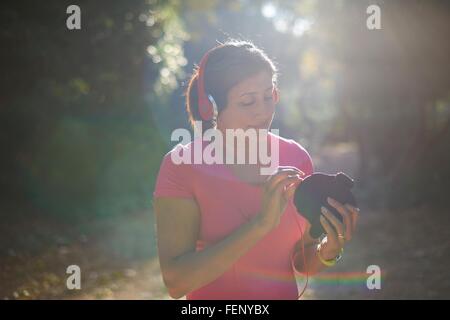 Donna matura che indossano le cuffie guardando in giù la preparazione di fascia da braccio Foto Stock