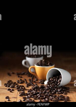 I chicchi di caffè in tazze da caffè che si rovescia sulla tavola di legno Foto Stock