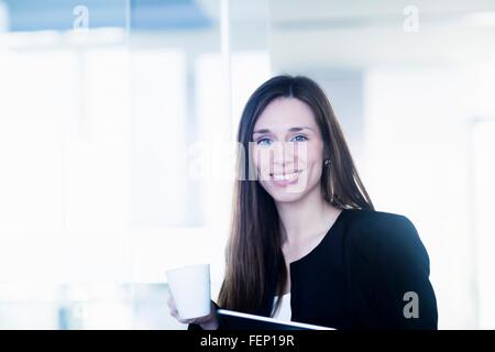 Giovane donna azienda tazza di caffè e ring binder file guardando sorridente della fotocamera Foto Stock