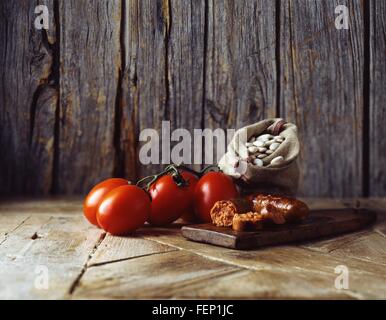 Roma pomodori sul vitigno, il Chorizo e il burro i fagioli in sacco di tela sul tagliere di legno Foto Stock