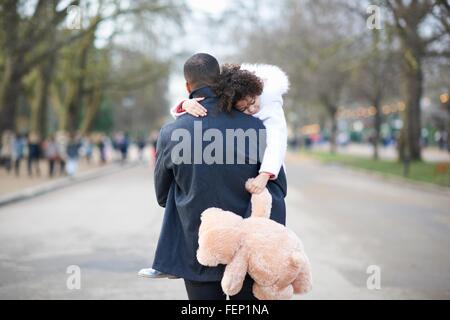 Vista posteriore del padre che porta la figlia a pelo holding peluche Foto Stock