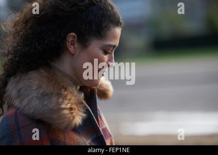 Vista laterale dei capelli ricci donna che indossa tartan rivestimento in pelliccia cappotto guardando giù sorridente Foto Stock