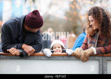 La ragazza con i genitori peeking sulla barriera, guardando alla fotocamera a sorridere