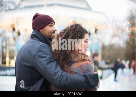 Vista posteriore metà uomo adulto che indossa knit hat con braccio attorno alla giovane donna che guarda lontano sorridente Foto Stock