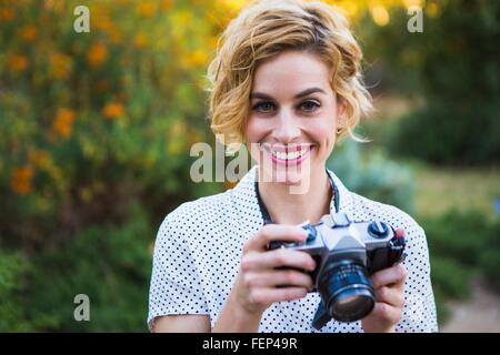 Ritratto di metà donna adulta holding fotocamera reflex, sorridente Foto Stock