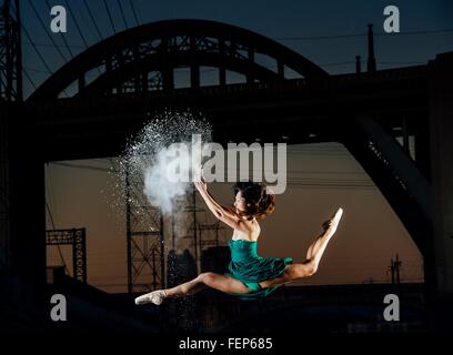 Giovane ballerino femmina saltando mentre il rilascio di esplosione di polvere al tramonto, Los Angeles, Stati Uniti d'America Foto Stock