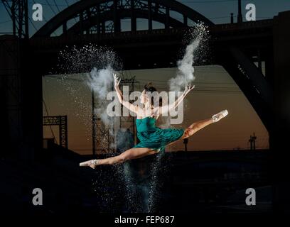 Femmina danzatore di balletto saltando mentre il rilascio di esplosione di polvere al tramonto, Los Angeles, Stati Uniti d'America Foto Stock