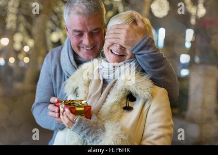 Uomo maturo consegna con il regalo di Natale alla moglie sul viale alberato, Maiorca, SPAGNA Foto Stock