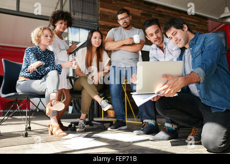 Avvio del lavoro di squadra e la pianificazione in riunione. Un gruppo di giovani uomini e donne guardando il portatile in ufficio. Foto Stock