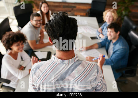 Vista posteriore del ritratto di uomo che spiega le idee di business per i colleghi durante una riunione nella sala conferenze. I giovani riuniti in Foto Stock