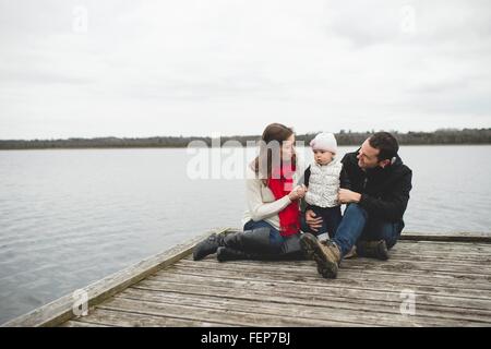 Famiglia giovane seduti insieme sul molo Foto Stock