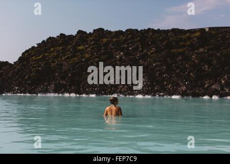 Vista posteriore della metà donna adulta Waist Deep in acqua, Laguna Blu hot springs, Islanda Foto Stock