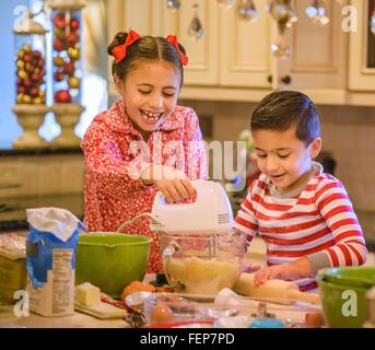 Bambini in cucina indossando pigiami mediante miscelatore a mano sulla pasta biscotto sorridente Foto Stock