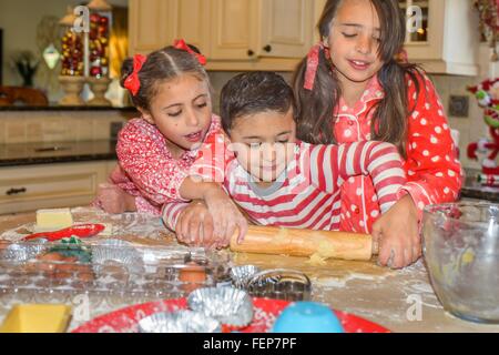 Bambini in cucina indossando pigiami di stendere la pasta con il mattarello Foto Stock