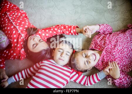 Vista aerea di bambini indossare pigiami giacente su un tappeto tenendo le mani gli occhi chiusi Foto Stock