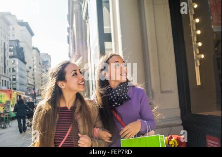Giovani adulti femmine gemelli con borse per lo shopping cercando fino alla finestra del negozio Foto Stock
