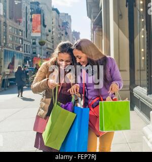 Giovani adulti femmine gemelli cercando in borse per lo shopping al di fuori della città shop Foto Stock