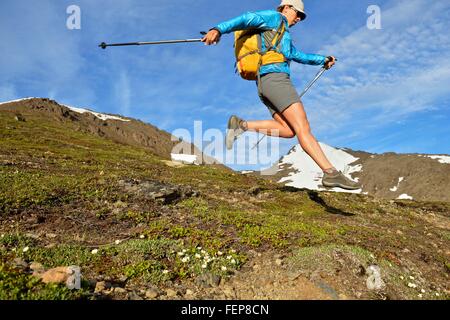 Femmina scalatore di montagna jumping in discesa, Chugach State Park, Anchorage, Alaska, STATI UNITI D'AMERICA Foto Stock