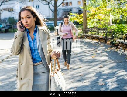 Giovane donna in chat sullo smartphone mentre a piedi attraverso il parco della città Foto Stock