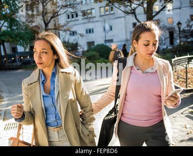 Giovane femmina adulta gemelli camminando sotto braccio attraverso il parco della città Foto Stock